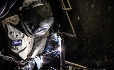 Welder in protective gear working with sparks flying during metal fabrication