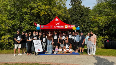 Large group photo at CARSTAR event with red tent, balloons, and diverse participants outdoors