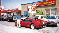 Red sports car parked outside auto collision repair shop with vintage vehicles
