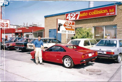Red sports car parked outside auto collision repair shop with vintage vehicles