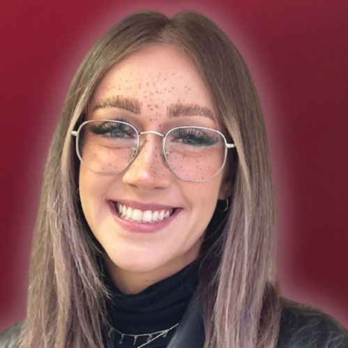 Smiling woman with glasses and freckles against burgundy background
