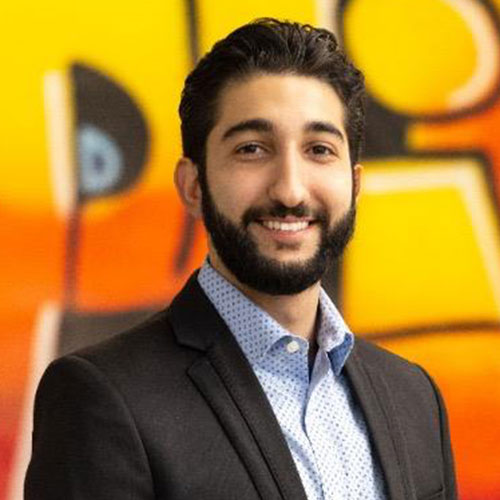 Smiling professional in black suit and patterned shirt against colorful background