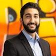 Smiling professional in black suit and patterned shirt against colorful background