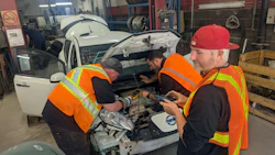 Auto mechanics in safety vests repairing a white vehicle in a garage workshop