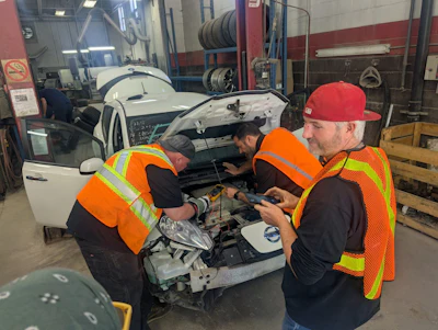 Auto mechanics in safety vests repairing a white vehicle in a garage workshop