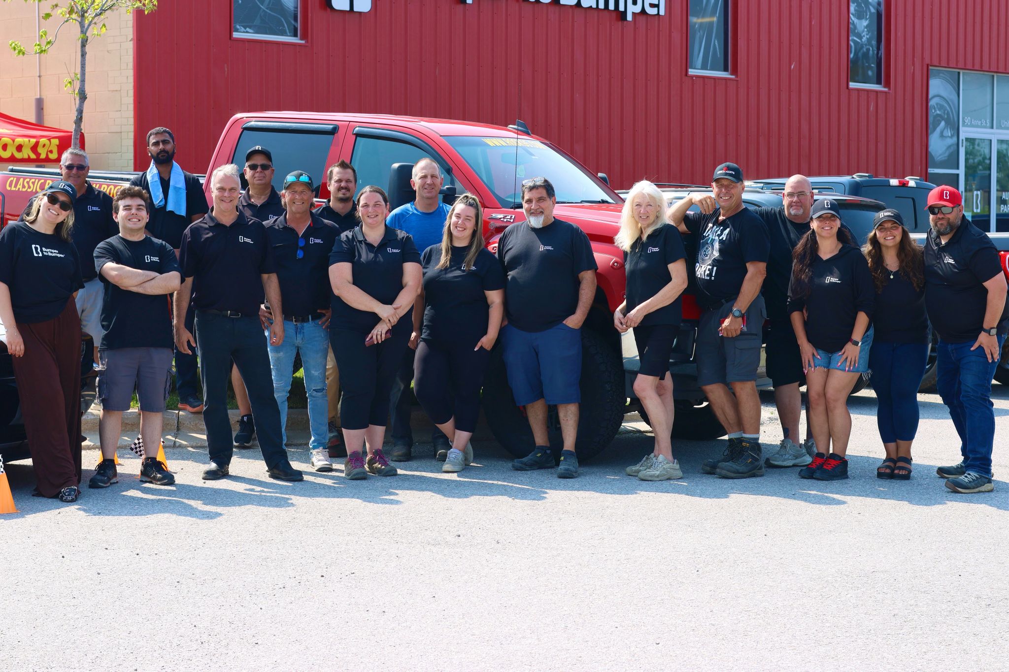 Diverse team of employees posing together in front of a red building and red truck