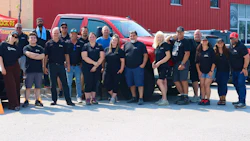 Diverse team of employees posing together in front of a red building and red truck