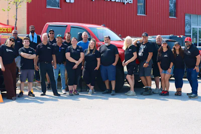 Diverse team of employees posing together in front of a red building and red truck