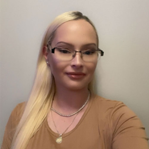 Woman with long blonde hair and glasses wearing a tan shirt