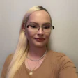 Woman with long blonde hair and glasses wearing a tan shirt
