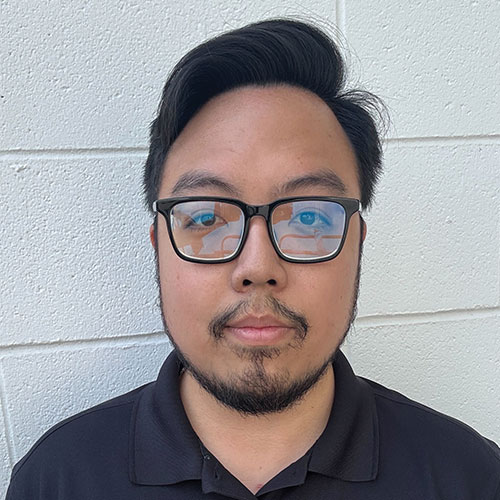 Professional headshot of a person wearing black-rimmed glasses and a dark polo shirt