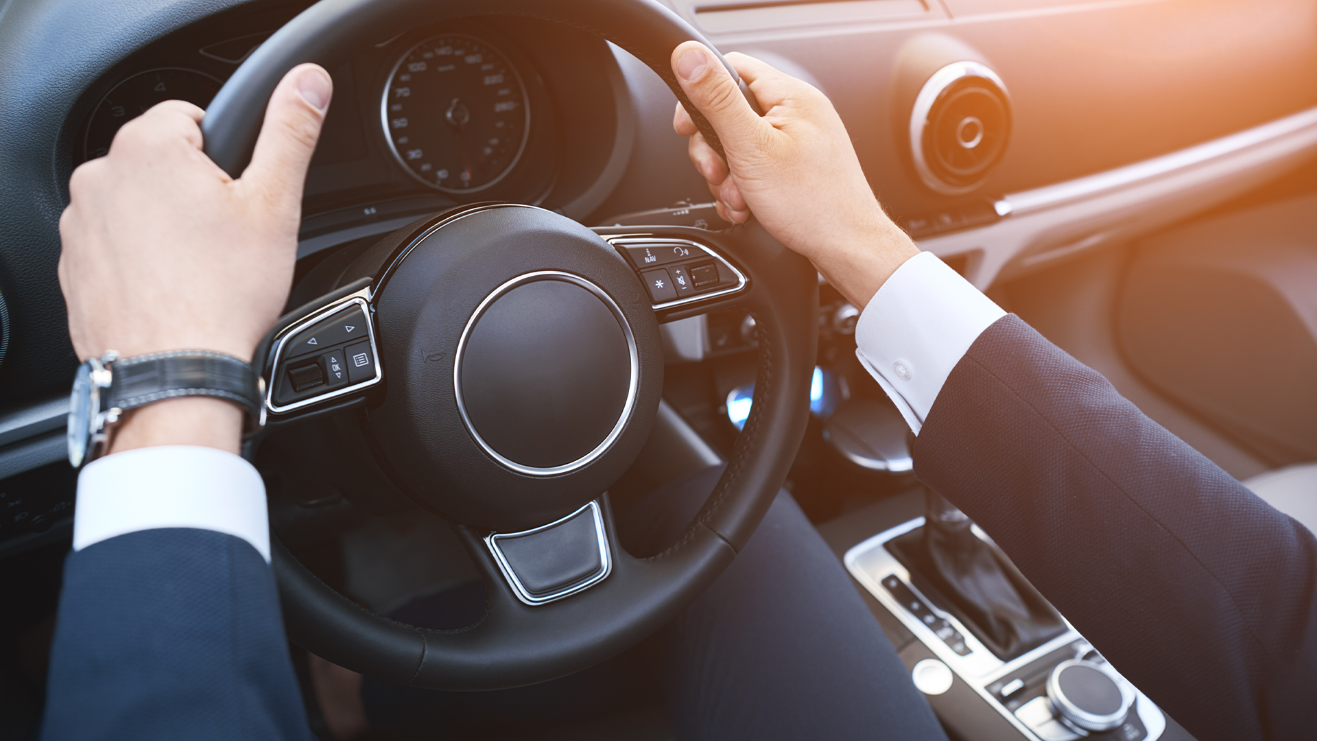 Hands on steering wheel of luxury car with dashboard and controls visible