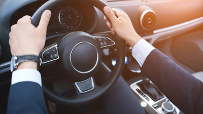 Hands on steering wheel of luxury car with dashboard and controls visible