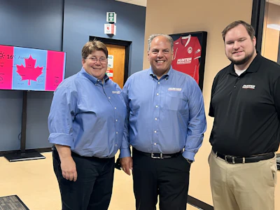 Three Hunter employees in blue and black shirts standing in an office with Canadian map display