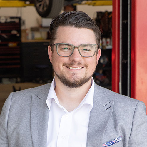 Smiling professional in gray blazer and glasses standing in automotive workshop