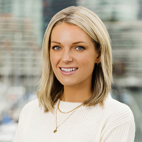 Smiling blonde professional woman in white sweater against blurred office background