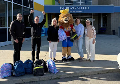 School mascot and staff posing with backpacks outside Jan Reimer School entrance