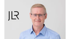 Professional headshot of a smiling middle-aged man in blue shirt with JLR logo