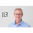 Professional headshot of a smiling middle-aged man in blue shirt with JLR logo
