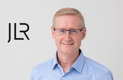 Professional headshot of a smiling middle-aged man in blue shirt with JLR logo