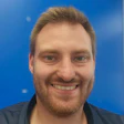Smiling man with beard in blue shirt against blue background