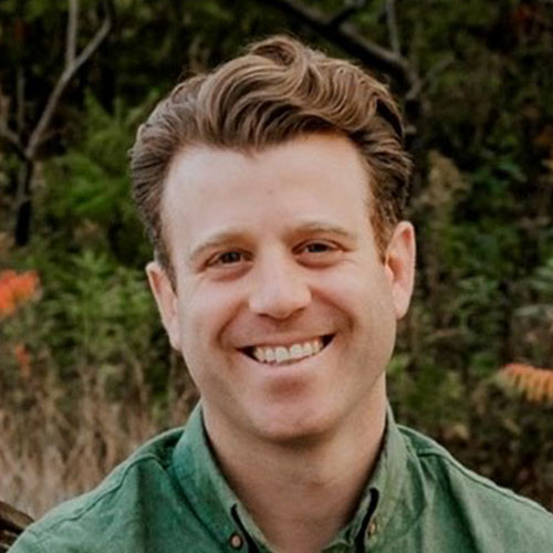 Smiling man in green shirt outdoors with trees in background