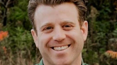 Smiling man in green shirt outdoors with trees in background