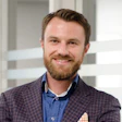 Smiling professional in plaid blazer and blue shirt against white background