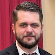 Professional man with beard wearing suit and tie, standing in front of red curtain