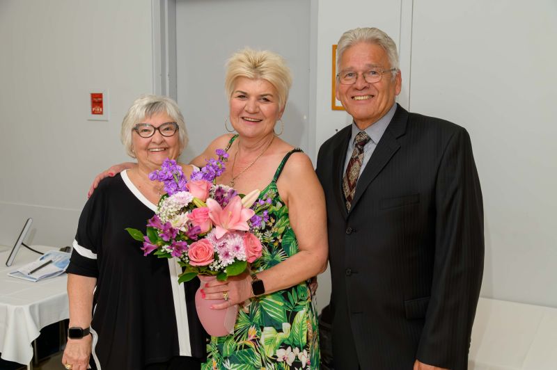 Three older adults smiling together, woman holding colorful flower bouquet