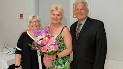 Three older adults smiling together, woman holding colorful flower bouquet