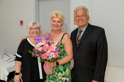 Three older adults smiling together, woman holding colorful flower bouquet