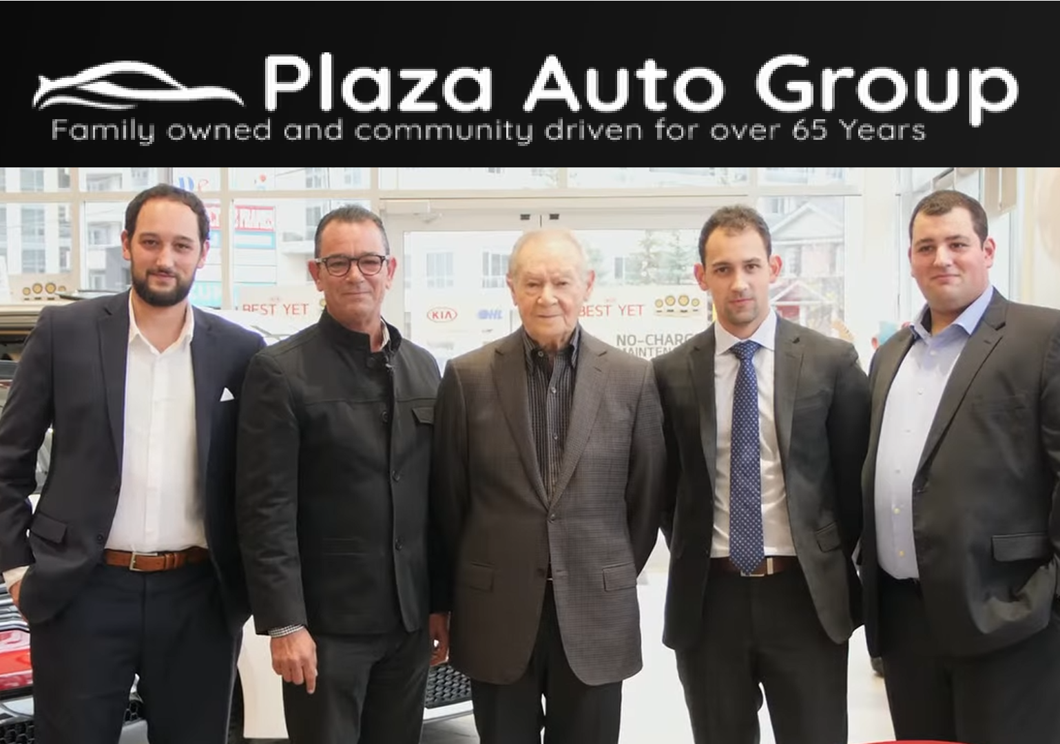 Five men in business attire standing in Plaza Auto Group dealership showroom