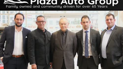 Five men in business attire standing in Plaza Auto Group dealership showroom