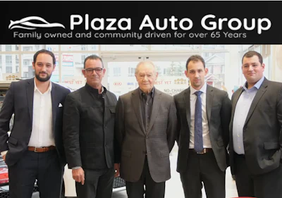 Five men in business attire standing in Plaza Auto Group dealership showroom