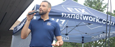 Man speaking into microphone at nxnetwork outdoor event tent