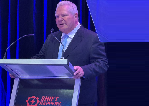 Speaker at Shift Happens conference presenting at a blue-lit podium