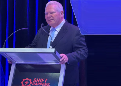 Speaker at Shift Happens conference presenting at a blue-lit podium