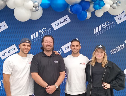 Four team members posing at 427 Auto corporate event with blue and white balloon backdrop