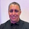 Professional man in black suit smiling against soft purple background