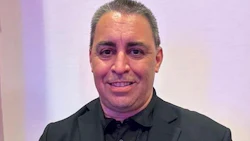 Professional man in black suit smiling against soft purple background