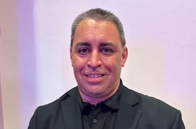 Professional man in black suit smiling against soft purple background