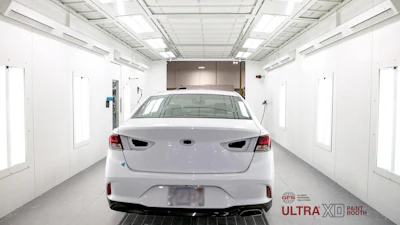 White car positioned inside a clean, modern automotive paint booth