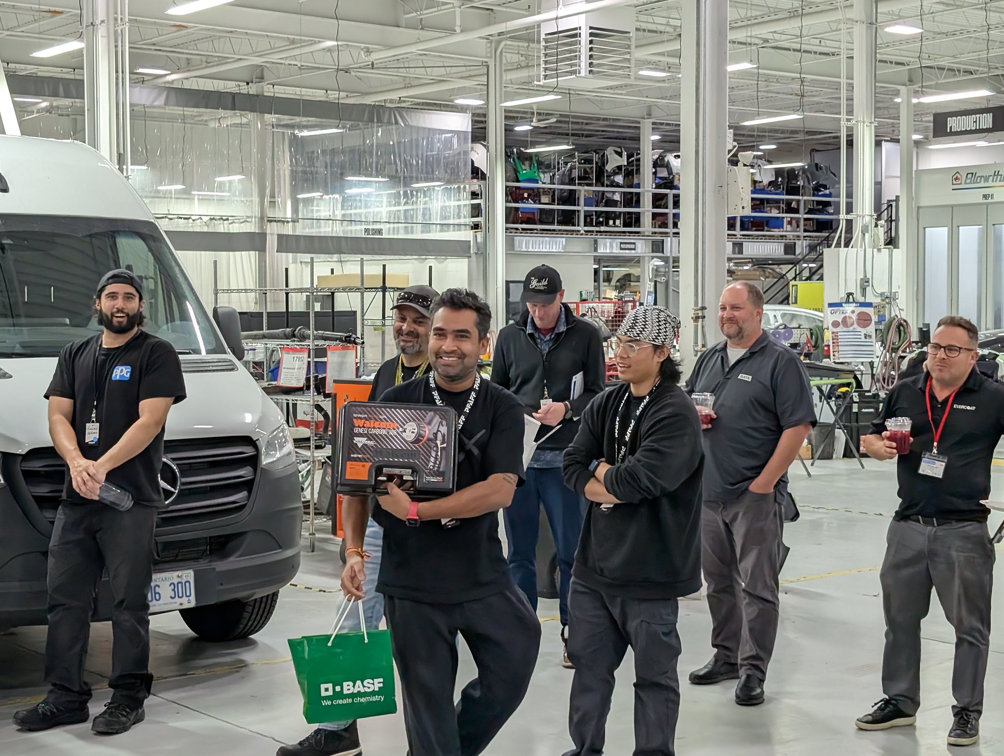 Team of workers standing near a white van in an industrial manufacturing facility
