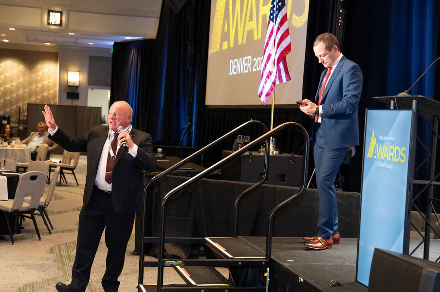Two speakers at Denver awards event with American flag and event backdrop