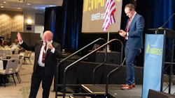 Two speakers at Denver awards event with American flag and event backdrop