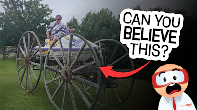 Person seated on vintage wooden wagon with large wheels in grassy outdoor setting