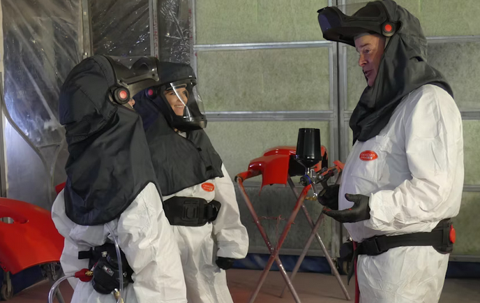 Three workers in white hazmat suits and protective hoods in industrial setting