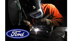 Ford logo near welder in orange jacket performing precision metal welding