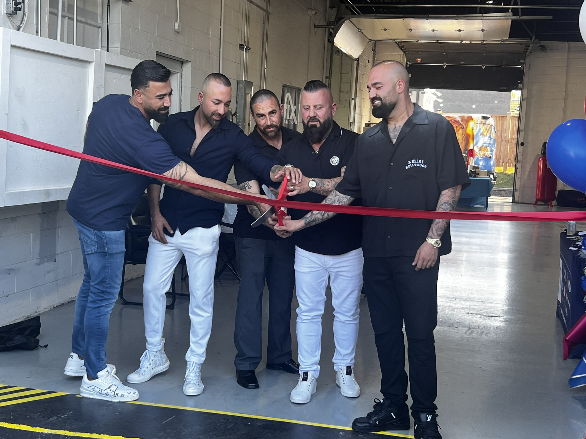 Five men cutting a red ribbon at a business opening or launch event